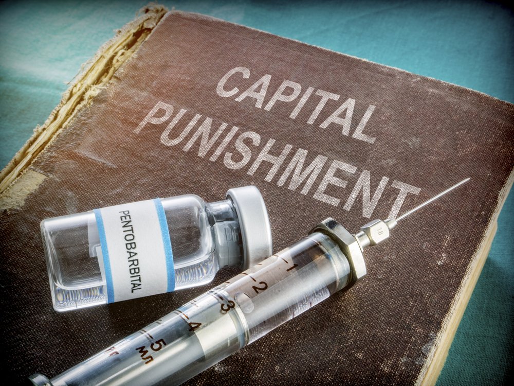 A deadly syringe laying on top of a book about capital punishment.