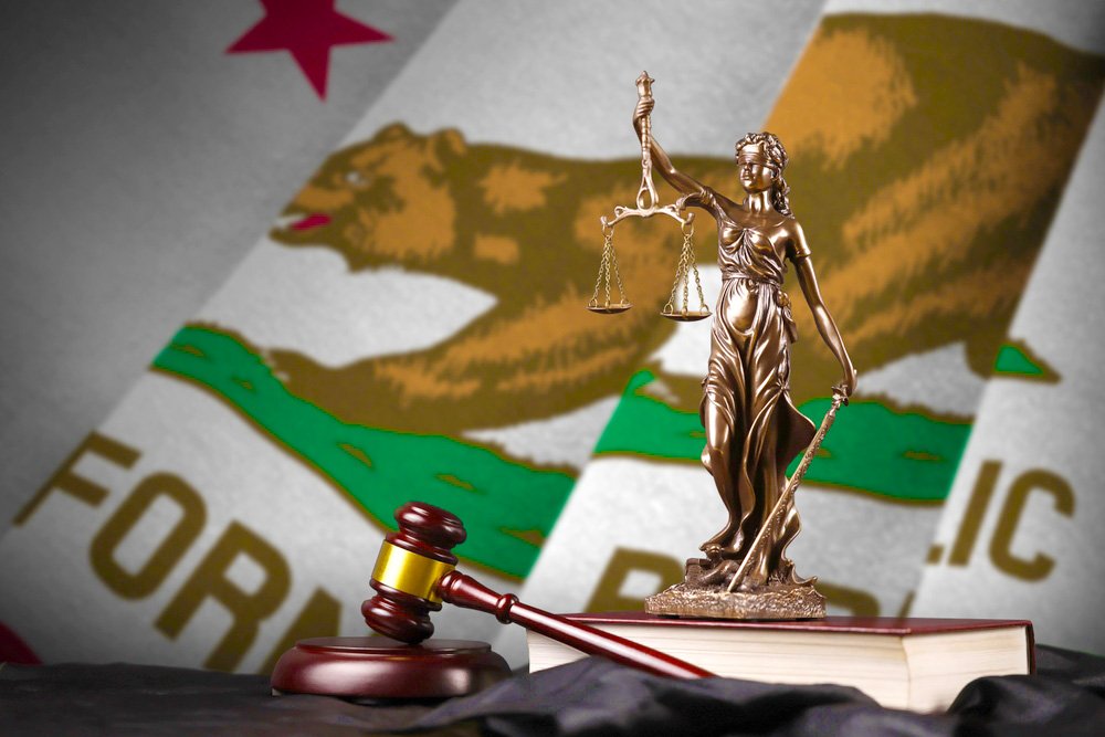 A statue of Lady Justice in front of the California state flag.