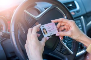 Two hands holding a driver's license against a steering wheel