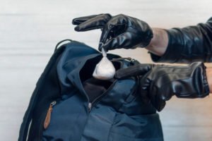 Gloved hands planting drugs into a backpack