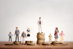 A conceptual piece representing wage discrimination, featuring members of different genders and age groups standing on differing amounts of money.