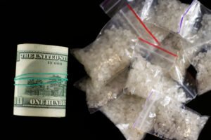 Bolsas llenas de metanfetamina al lado de un rollo de billetes de cien dólares.