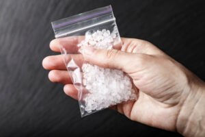 A person holding a baggie filled with rocks of methamphetamine.