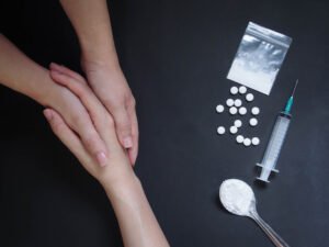 Counselor holding hand of drug addict with syringe and pills next to them