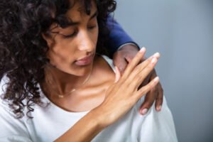 A man wearing a business suit puts his hand on the shoulder of a young female employee. She pushes his hand away.