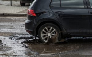 Car hitting pothole in city street splashing muddy water.