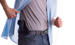 Man pulling back shirt revealing gun in waist of jeans