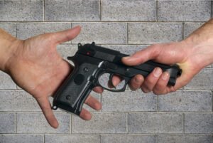 Hand holding a revolver giving it to another hand against a cinder block wall