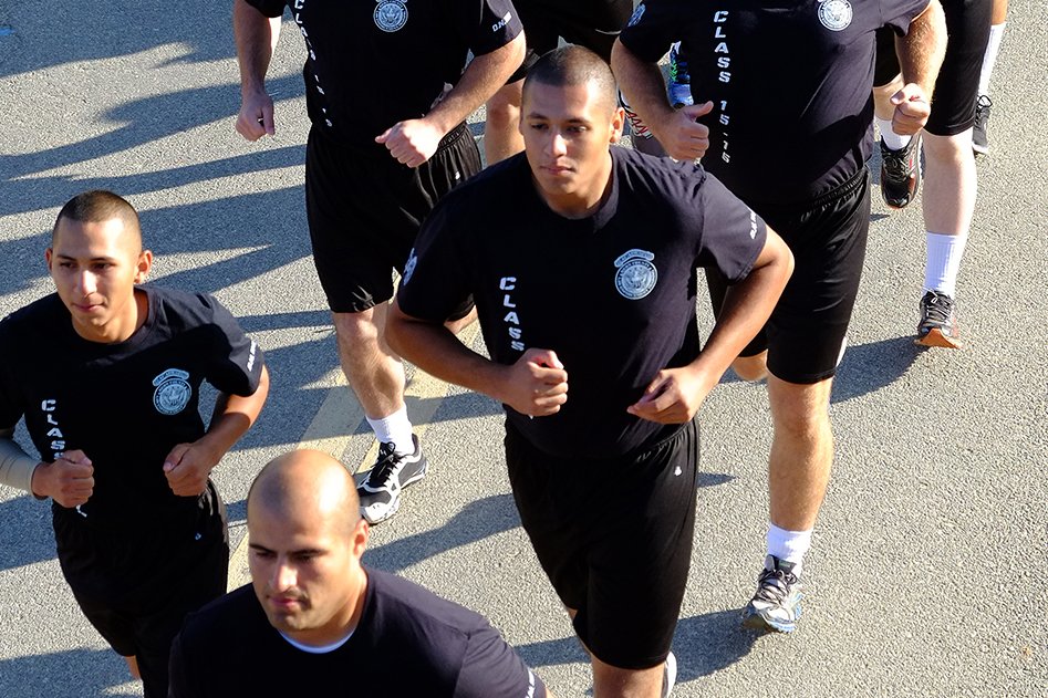 Police academy cadets wearing t-shirts with printed police officer badges, jogging in formation on a city street