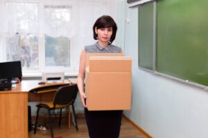 Teacher with box of belongings leaving her desk after getting fired