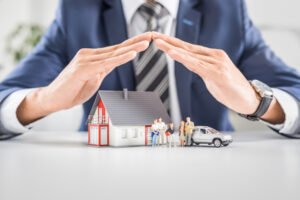 Insurance agent tenting hands over a small house, car, and family