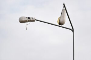 View of two broken streetlights hanging loosely by wires on metal poles, with grey sky in background