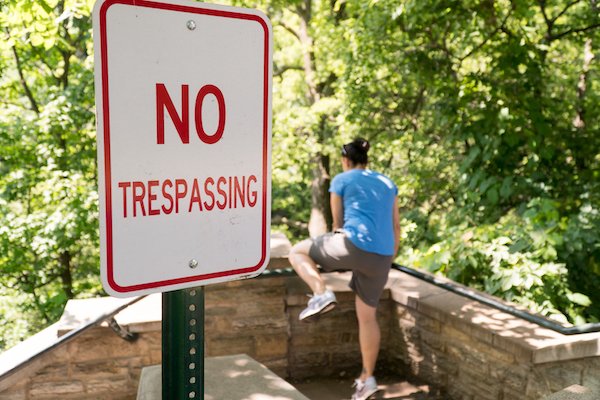 Persona cruzando una barrera detrás de un letrero de "no trespassing"