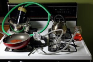Crudely constructed meth lab on a stove top consisting of crushed nasal decongestant pills, mysterious solutions, a red powder, pots and pans, and hoses