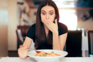 Mujer comiendo en un restaurante mientras se cubre la boca con la mano en disgusto