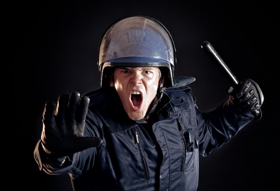 Angry police officer with nightstick telling the violent crowd to stop