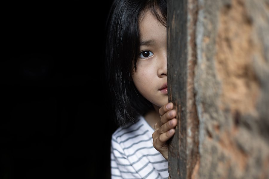 Child looking scared hiding behind wall