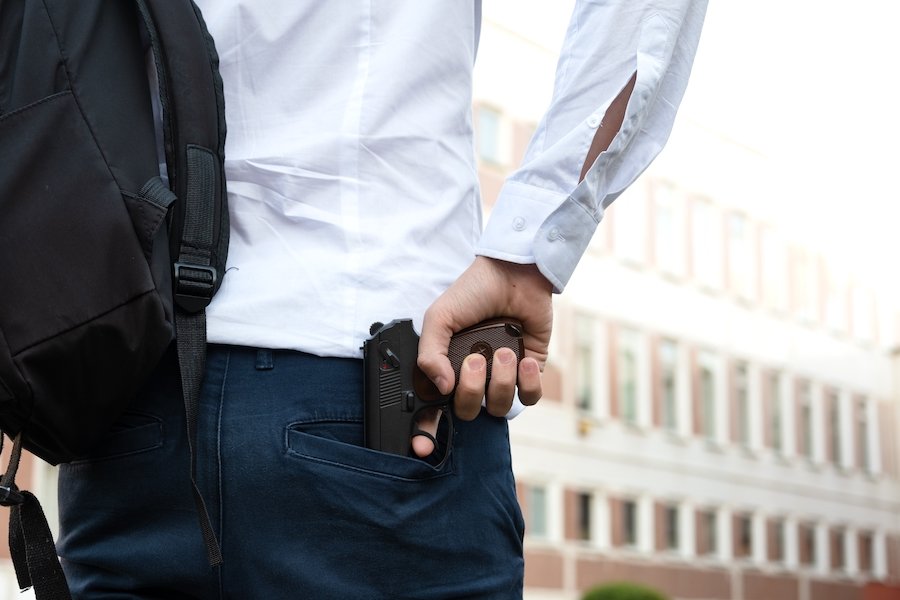 Hombre sosteniendo un arma fuera de un edificio universitario